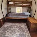 Interior of wagon. Bunkbed with queen on the bottom and twin mattress on top. view include a picture of throw rug on the floor and a table.