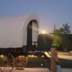 Exterior image of covered wagon during the moon rise in the background.