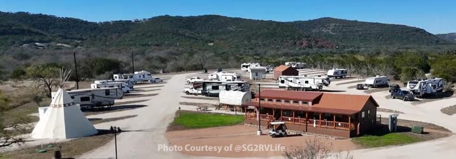 Arial photo taken by drone above ground of the park landscape. Clubhouse in foreground Tipi and RV travel trailers in spots.