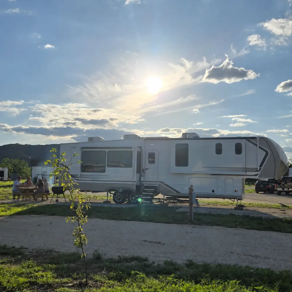 Guests enjoying a barbecue at a picnic table beside a large RV site at Pitmaster RV Park in Concan, Texas.