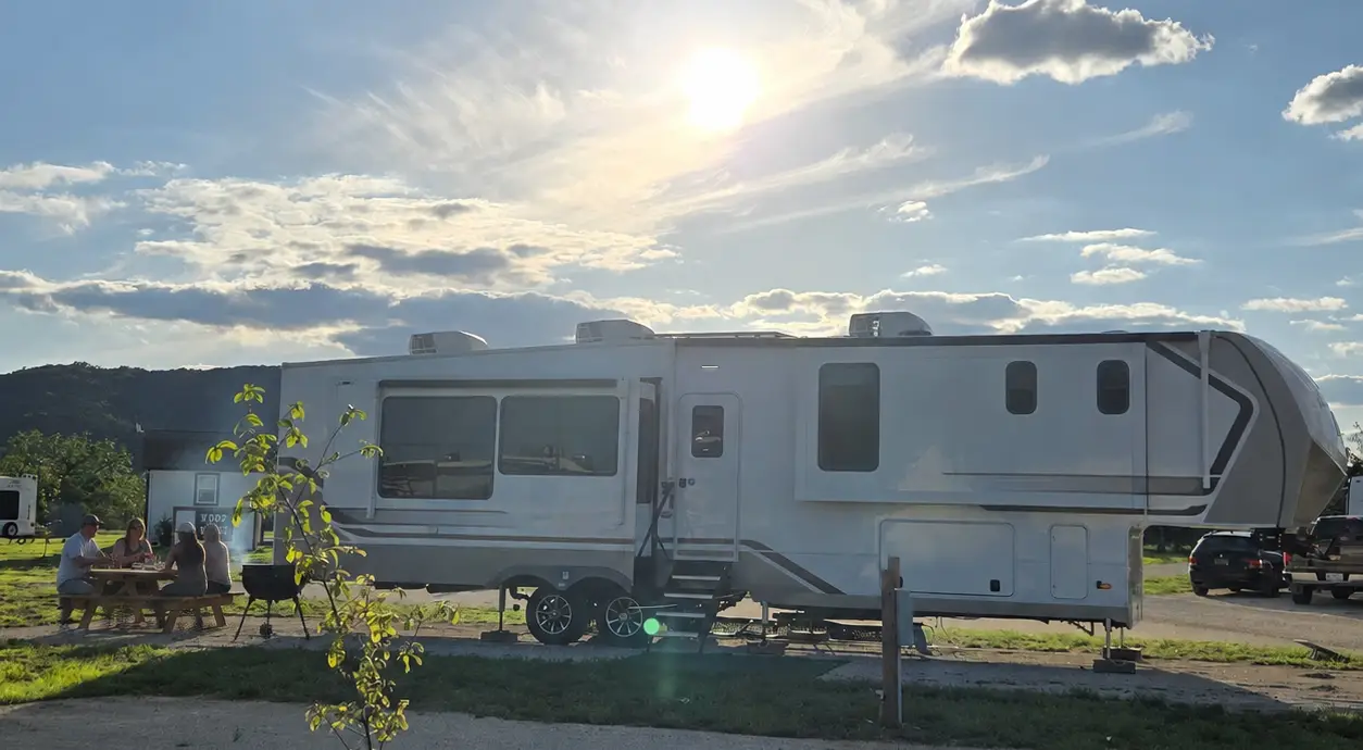 Guests enjoying a barbecue at a picnic table beside a large RV site at Pitmaster RV Park in Concan, Texas.