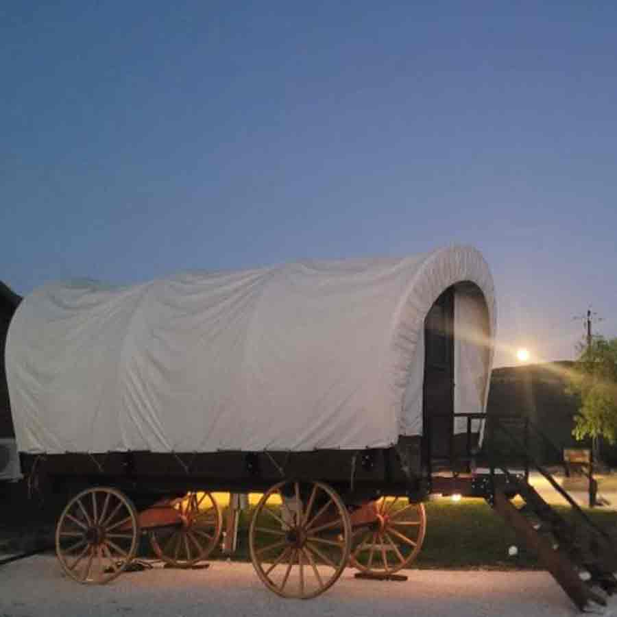 Covered wagon glamping accommodation at Pitmaster RV Park in Concan, Texas illuminated at dusk.