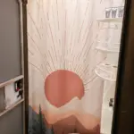 RV bathroom with a curved shower curtain showing a stylized sun over mountains, a toilet, and a skylight above.